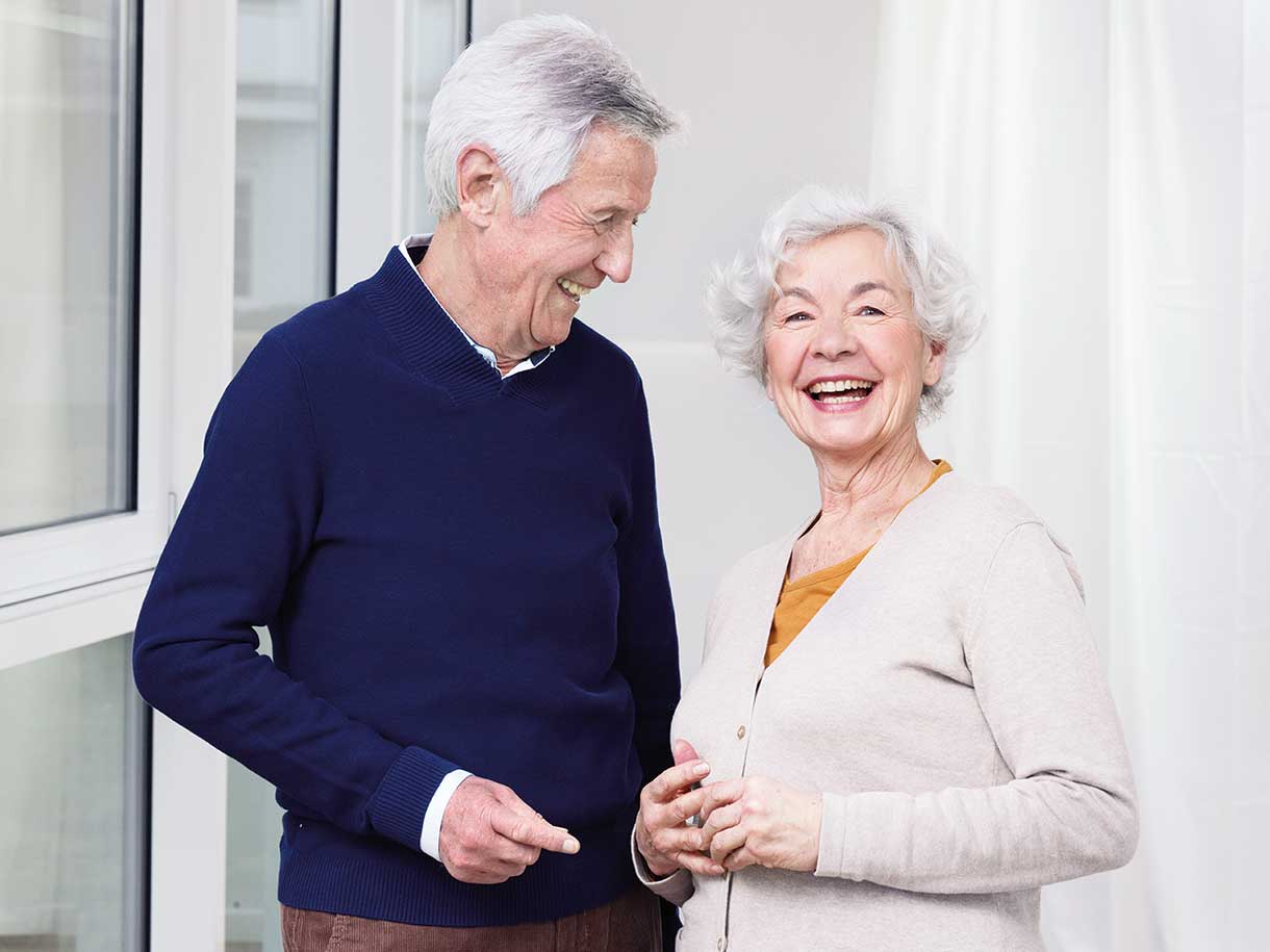 Um homem e uma mulher idosos em pé, lado a lado, sorrindo